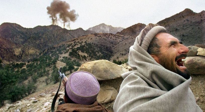Un combatiente afgano de la Alianza del Norte ríe a carcajadas mientras aviones estadounidenses atacan una posición talibán cerca de Tora Bora, Afganistán, en diciembre de 2001. Los líderes de las milicias afganas declararon la victoria en la batalla de Tora Bora y afirmaron haber capturado la última base de Al Qaeda.