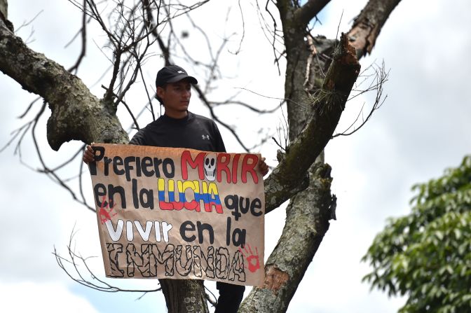 Un hombre sostiene un cartel que dice "Prefiero morir en la lucha que vivir en la inmunda" desde arriba de un árbol en la protesta contra la reforma fiscal en Cali, Colombia.