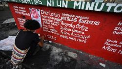 An artist writes the names of protesters who died during clashes with riot police, during a new protest against the government of President Ivan Duque triggered by a now abandoned tax reform, in Cali, Colombia, on May 8, 2021. - Facing anti-government protests that have spiralled into deadly violence, Colombian President Ivan Duque is holding a series of talks with his political foes in search of a way out of the crisis. (Photo by Luis ROBAYO / AFP)