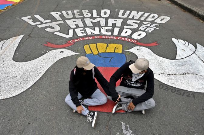 Dos manifestantes se toman de la mano frente a una pintura que dice "El pueblo unido jamás será vencido" en la Vía Panamericana, el principal corredor vial del país, en Valle del Cauca.
