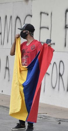 Un hombre sostiene una bandera de Colombia durante enfrentamientos de la policía antidisturbios en el sector de La Portada en Cali, Colombia. "Apoyamos el paro. No a la reforma", dice un grafiti en la pared detrás de él.