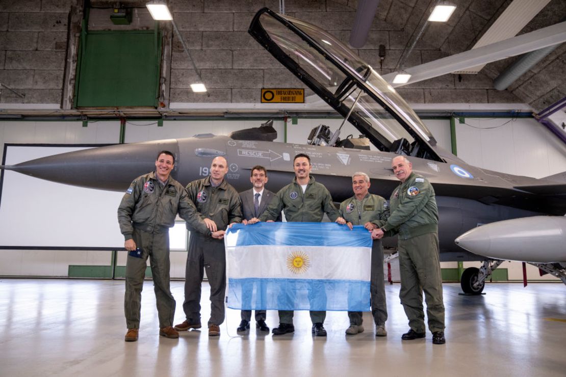 Miembros de la delegación argentina, incluido el ministro de Defensa Luis Alfonso Petri, sostienen la bandera nacional mientras delante de un caza F-16 tras la firma de un acuerdo sobre la compra de aviones F-16 daneses en la base aérea de Skrydstrup, Dinamarca, el 16 de abril de 2024.