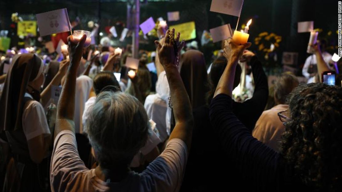 Gente levanta sus manos durante una oración en el sitio del memorial por las víctimas del edificio colapsado.