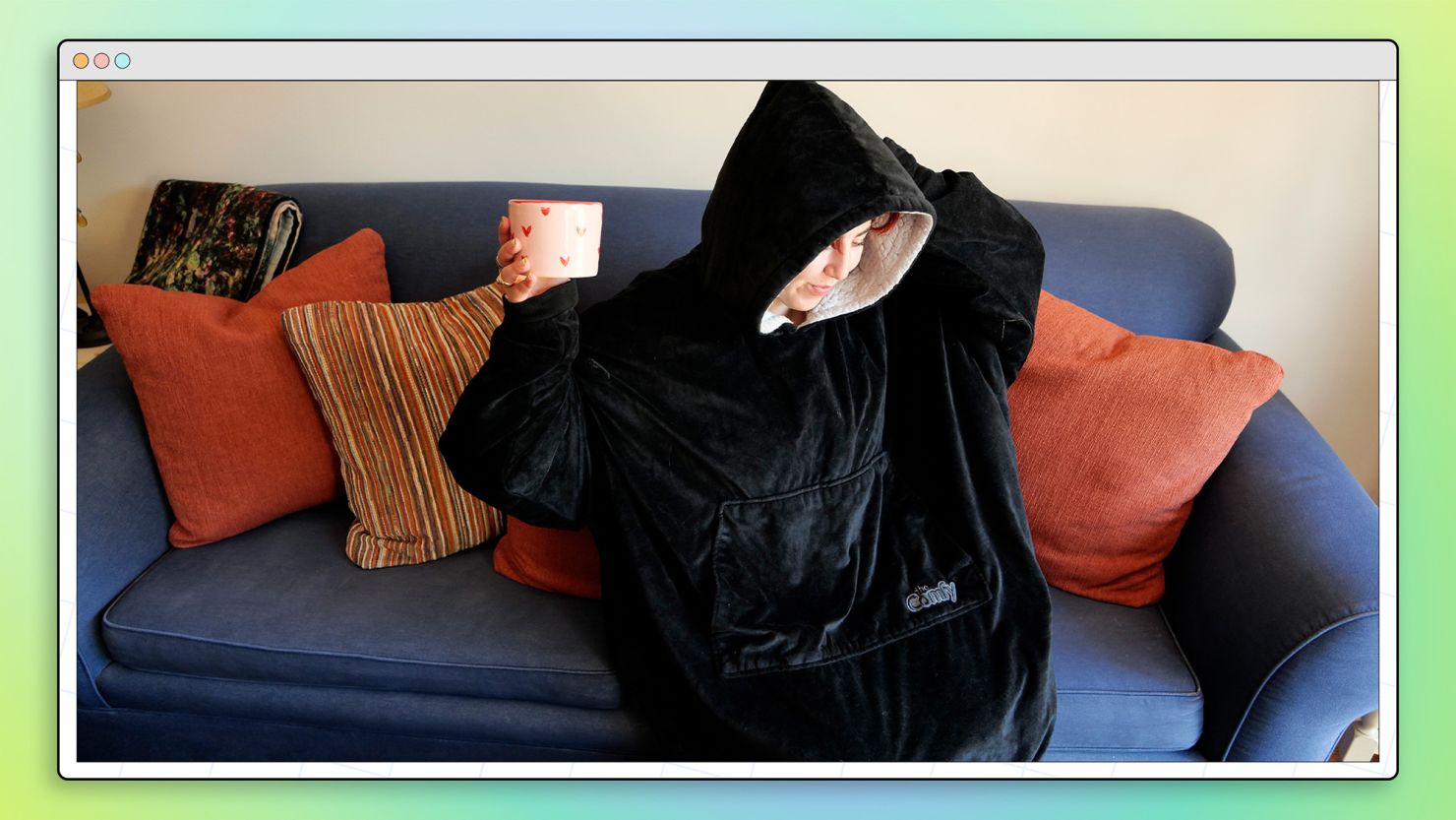 Woman sitting on couch wearing The Comfy (an oversized hoodie) holding a mug.