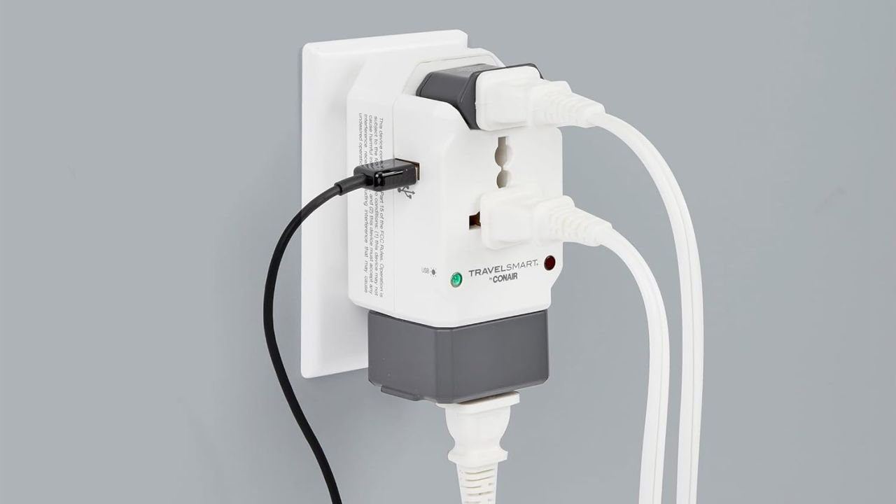 The Conair Universal Travel Adapter is plugged into a wall outlet and has three power cords and a USB cable plugged in.