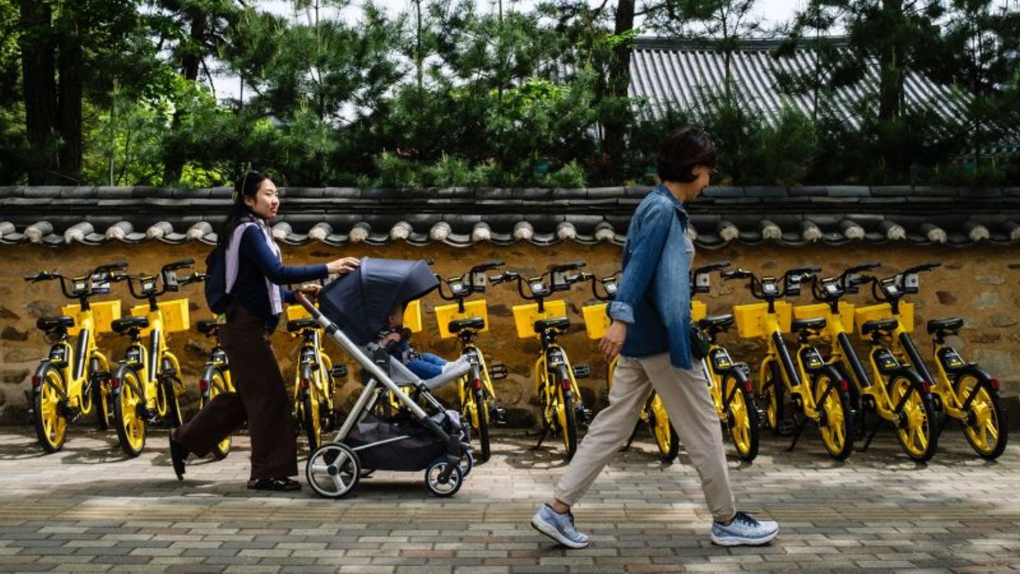 Una mujer empuja a su hijo en un cochecito junto a bicicletas de alquiler en Seúl el 26 de abril de 2024.