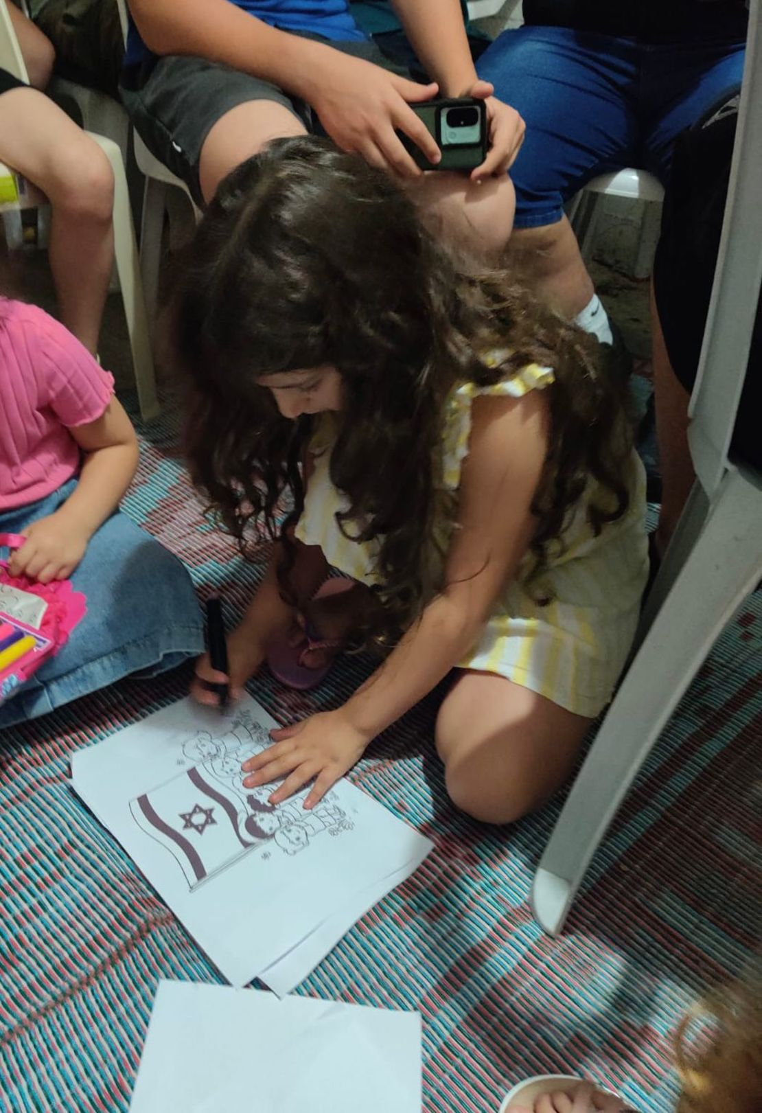 Young girl in a bomb shelter passes early morning hours by coloring on the floor.
