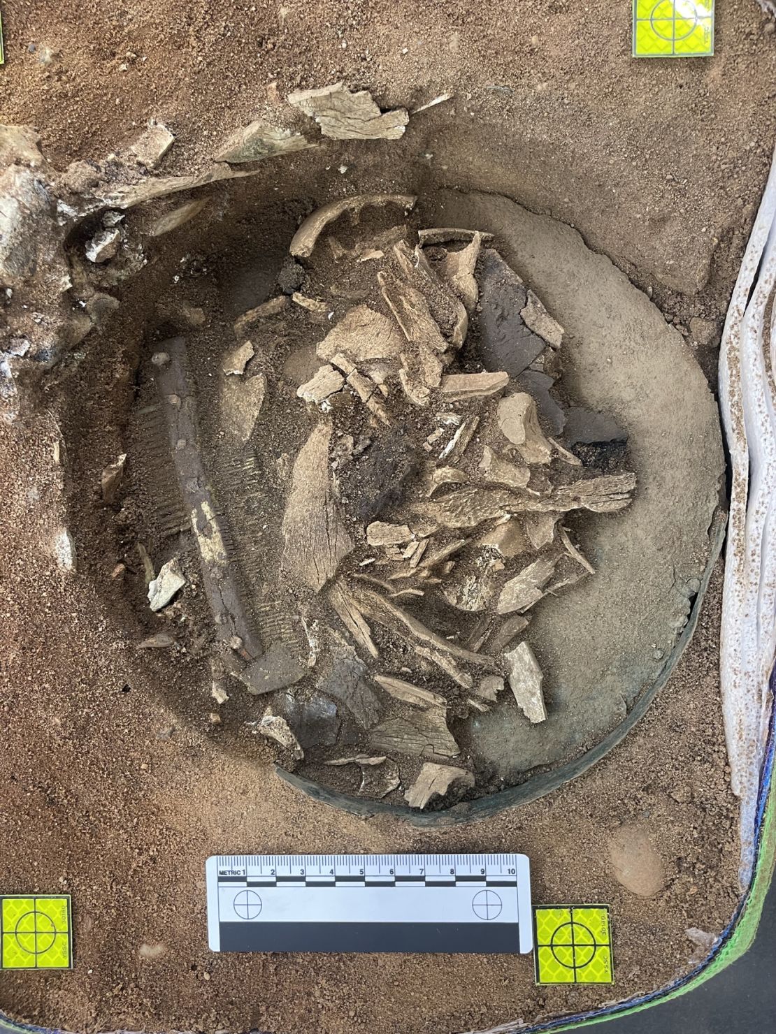 Cremated human and animal bones are seen within the bucket's base, along with a double-sided comb.