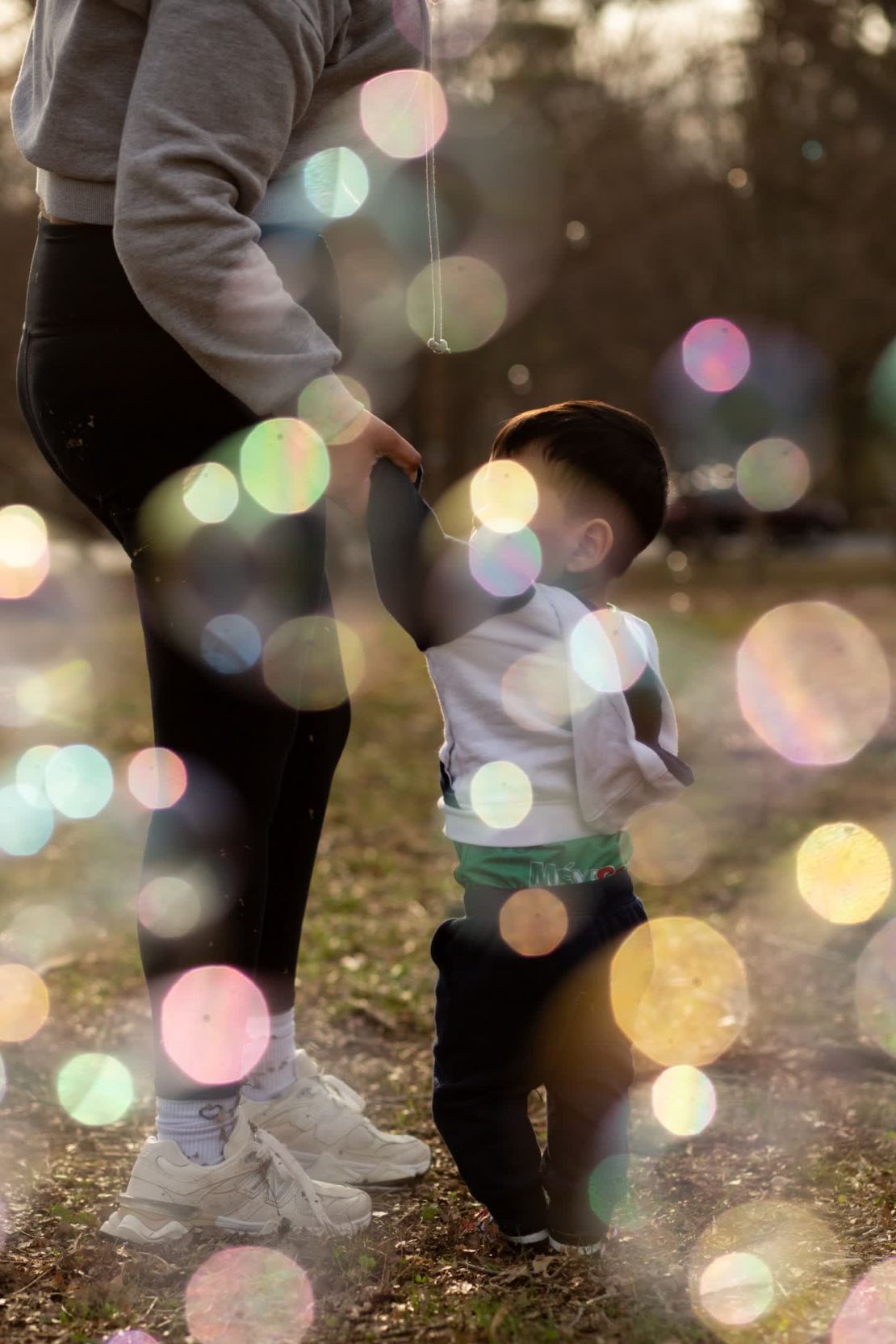 E y su hijo persiguen burbujas en el parque. Es una de las varias madres inmigrantes que la fotógrafa Emily Whitney ha estado siguiendo. Como les preocupa que hablar abiertamente pueda poner en peligro a sus familias, Whitney las identifica solo por sus iniciales y no muestra sus rostros.