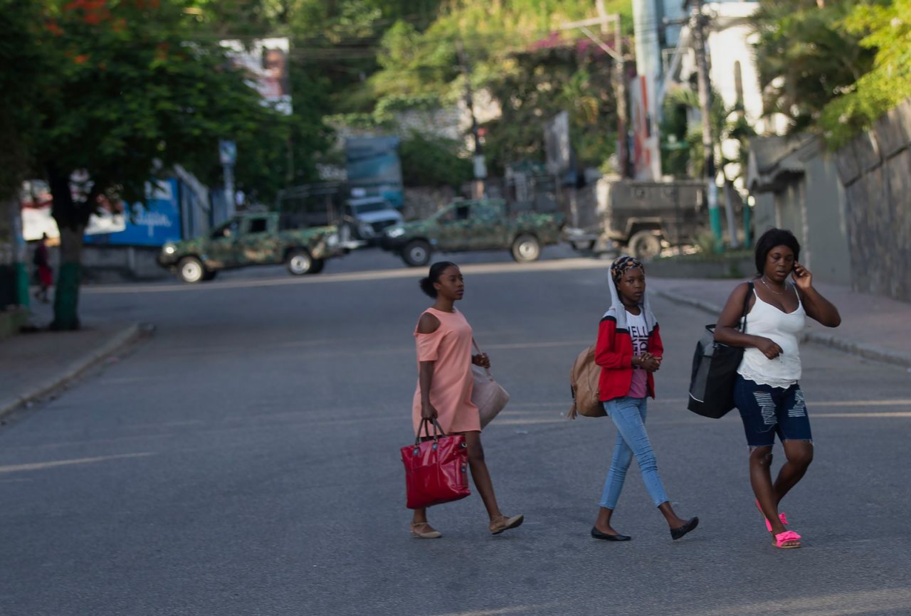 People walk past military vehicles blocking the entrance to Petion Ville, the neighborhood where the late Haitian President Jovenel Moise lived in Port-au-Prince on Wednesday.