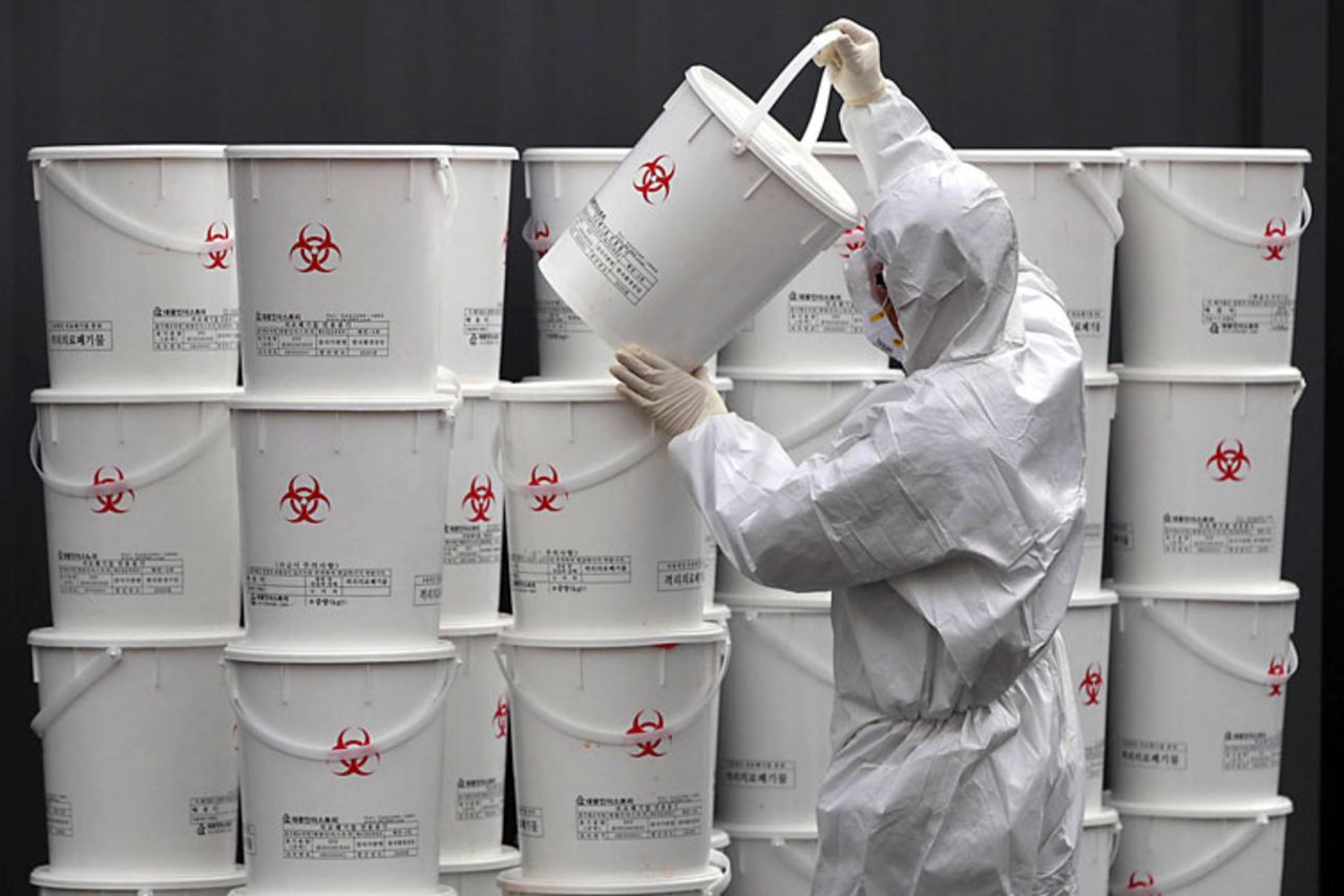 A worker in protective gear stacks plastic buckets containing medical waste from coronavirus patients at a medical center in Daegu, South Korea, Monday, February 24.