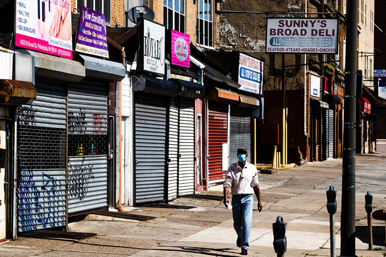 A person wearing a protective face mask as a precaution against the coronavirus walks past stuttered businesses in Philadelphia, on Thursday, May 7.