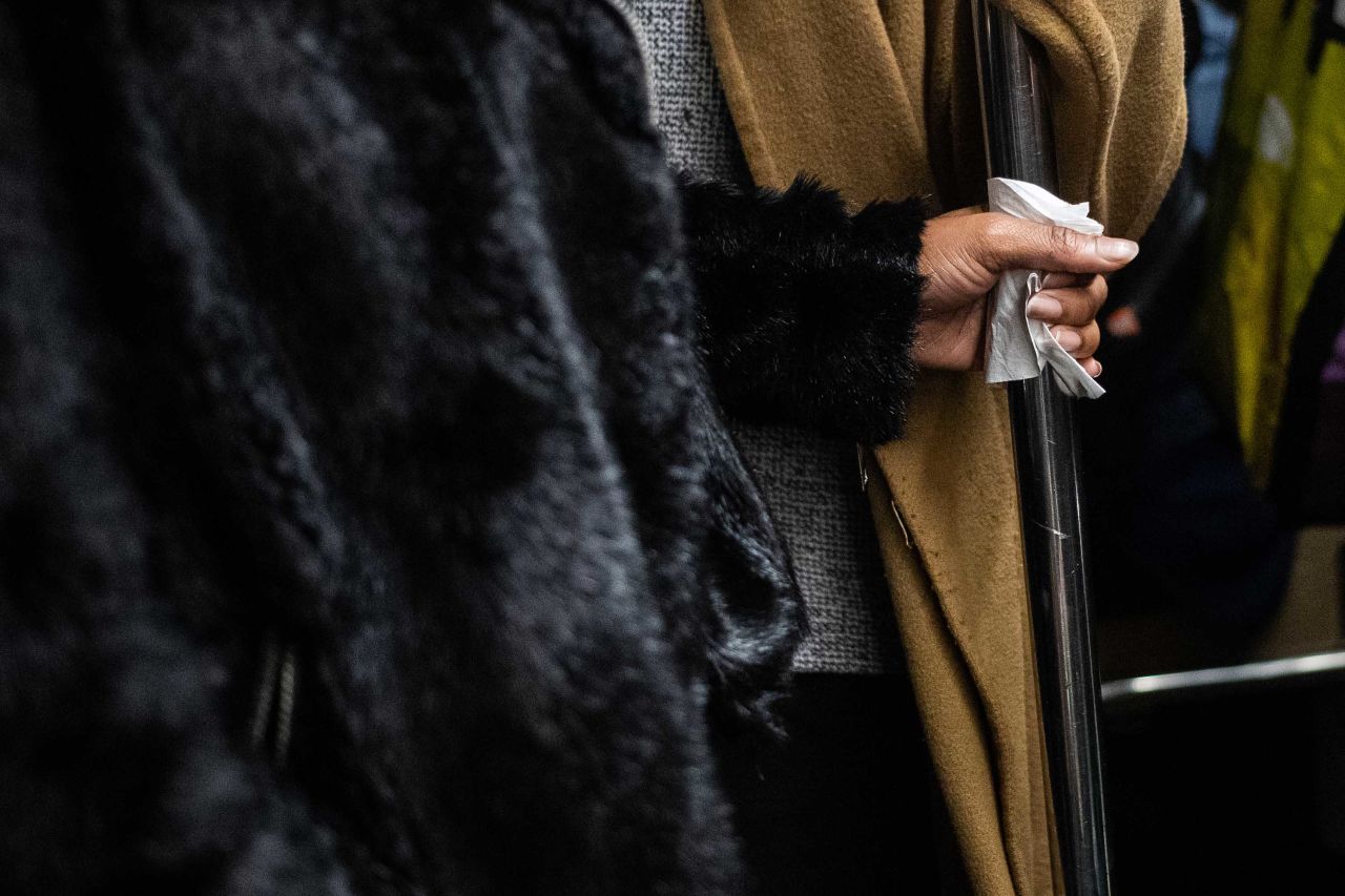 A subway passenger uses a tissue while holding a handrail on a train in New York City, on Tuesday.