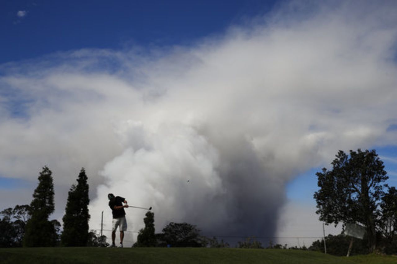 Mike Walls plays golf in Volcano, Hawaii as a huge ash plume rises from the summit of Kiluaea volcano Monday, May 21, 2018.