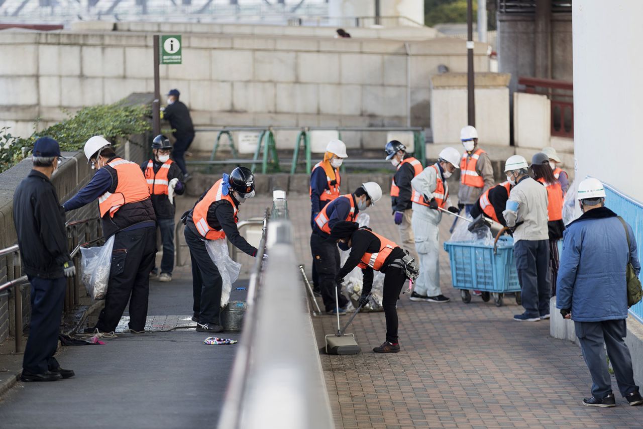 Mask-wearing custodians clean handrails and pick up trash near Sumida River in Tokyo on Friday, December 11.