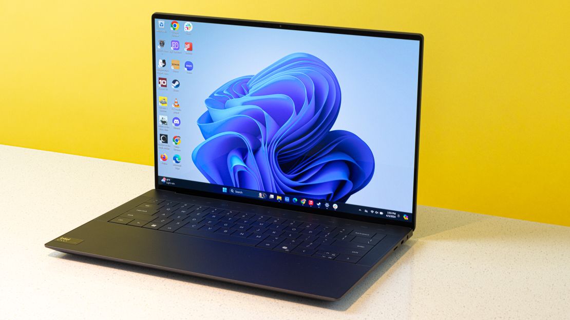 The Dell XPS 14 is open to a light blue Windows 11 desktop background design.