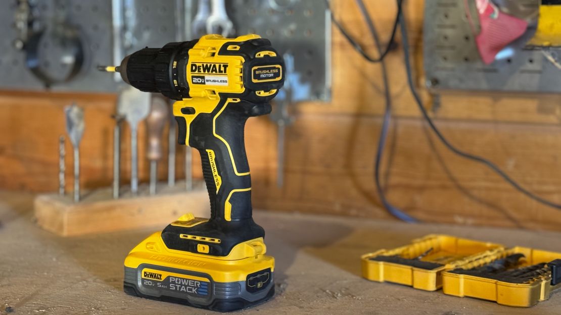 DeWalt drill placed on table in workshop, standing next to box of drills.