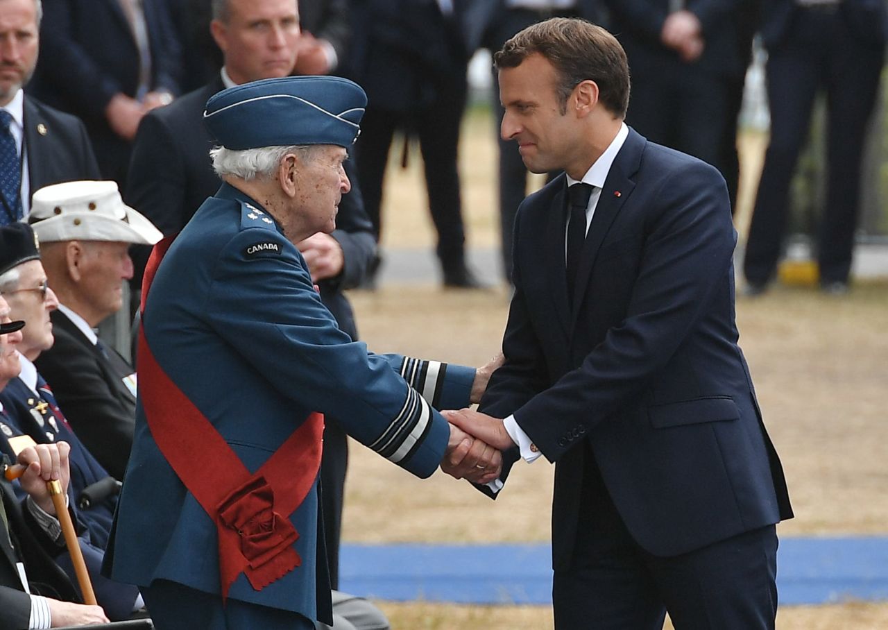 French President Emmanuel Macron shakes hands with a veteran as he takes his seat.