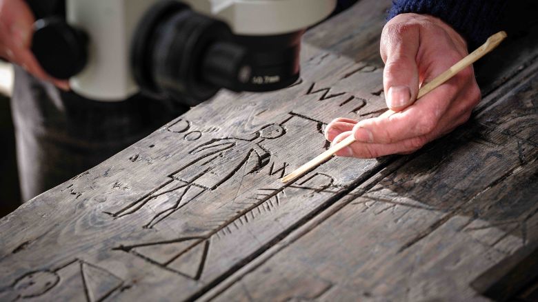 EMBARGOED 00.01 WEDNESDAY 15 MAY: A conservator examines over 50 pieces of graffiti on a door from the 1790s newly discovered by English Heritage at Dover Castle. With tensions high but hours to kill, soldiers on duty there guarding against the threat from Napoleon used knives or possibly bayonets to carve a cartoon-like snapshot of the time including a sailing ship, the date of the French revolution (1789), nine macabre depictions of hangings, and countless initials. The door has been conserved to go on display in July as part of ‘Dover Under Siege’ – a new experience which will open up the castle’s northern defences, including the medieval and Georgian underground tunnels and Georgian casemates, to visitors. Pictured: A hanging.