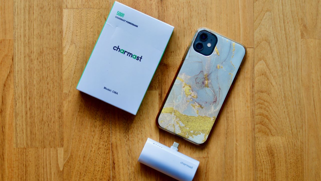 A photo of the Charmast Portable Phone Charger next to an iPhone and its retail packaging on a wooden table