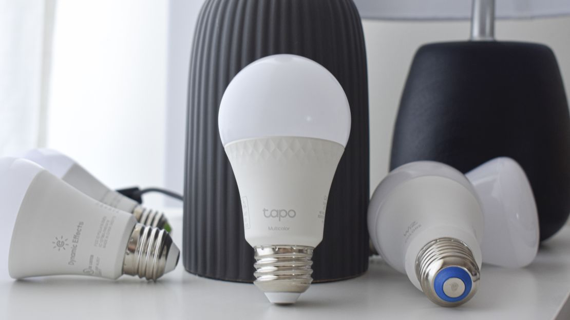 Several smart bulbs in front of a black lamp on a white table.