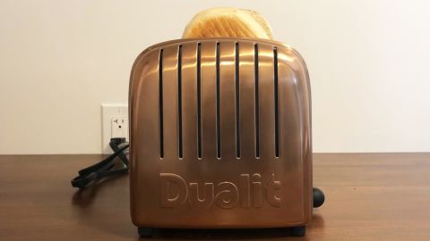 A copper-plated Dualit New Gen 2-Slice Toaster, toasting a bagel.
