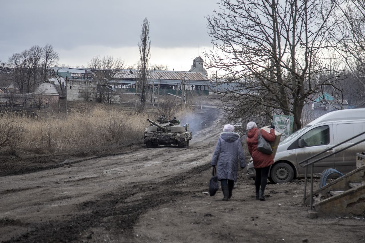 Civilians walk on a road as a tank drives by in a village nearby Avdiivka front line on February 20.