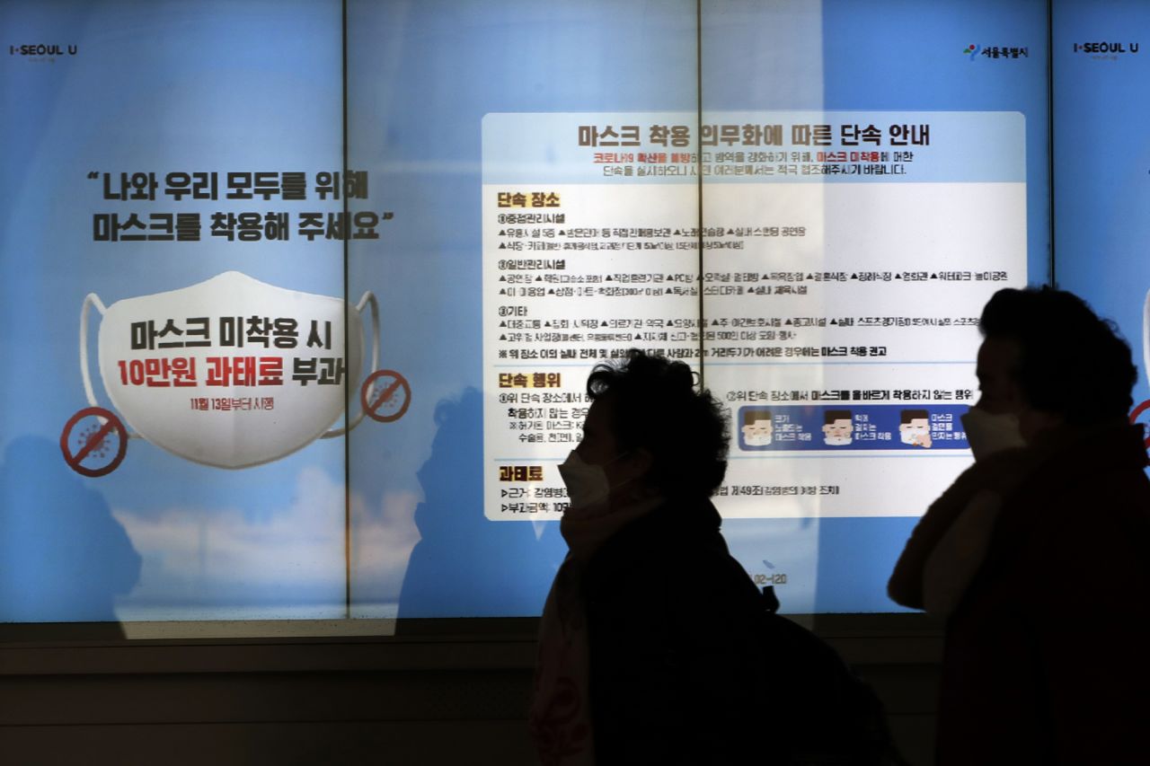 People wearing face masks walk near a screen displaying precautions against the coronavirus in Seoul, South Korea, on Sunday, December 27, 2020.