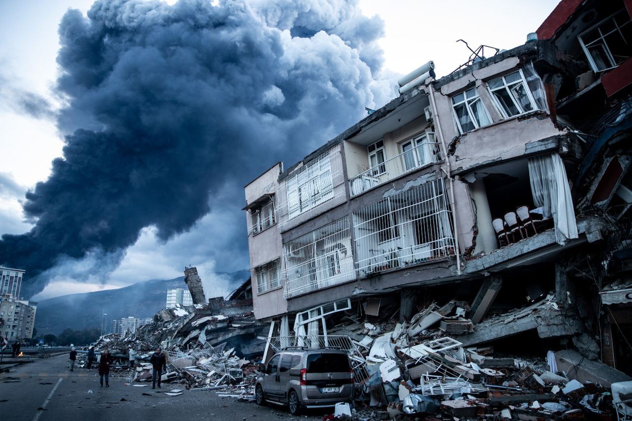 Smoke billows from a fire in Iskenderun port in Turkey as people walk past collapsed buildings on Tuesday.