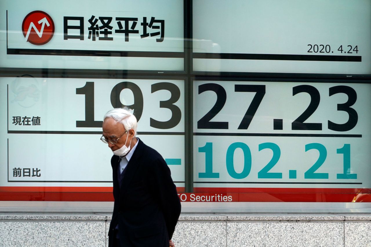 A man wearing a mask to help stop the spread of the new coronavirus walks past an electronic stock board showing Japan's Nikkei 225 index at a securities firm in Tokyo Friday, April 24.