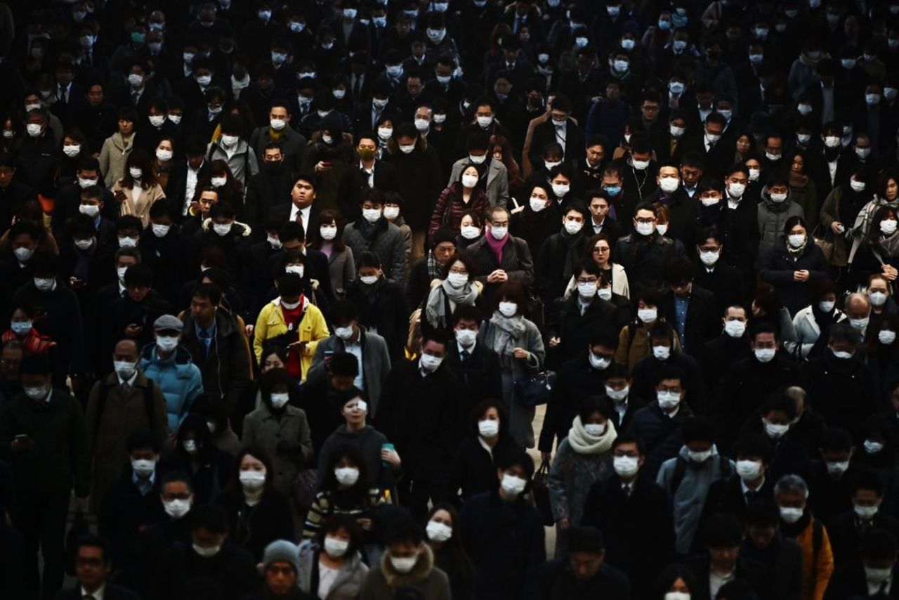 Mask-clad commuters make their way to work during morning rush hour in Tokyo today.