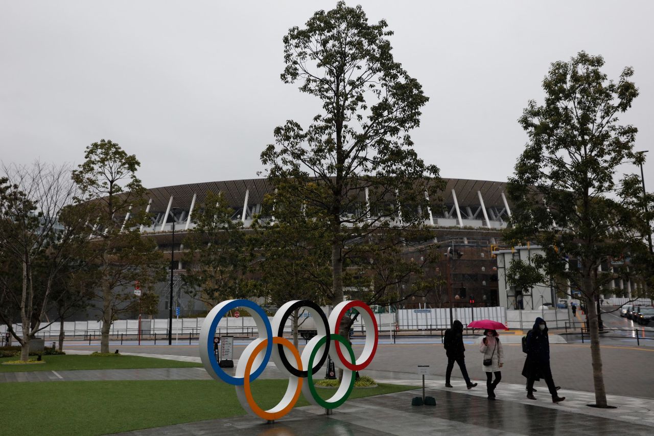 People walk past the Olympic rings near the New National Stadium in Tokyo, Wednesday, March 4. 