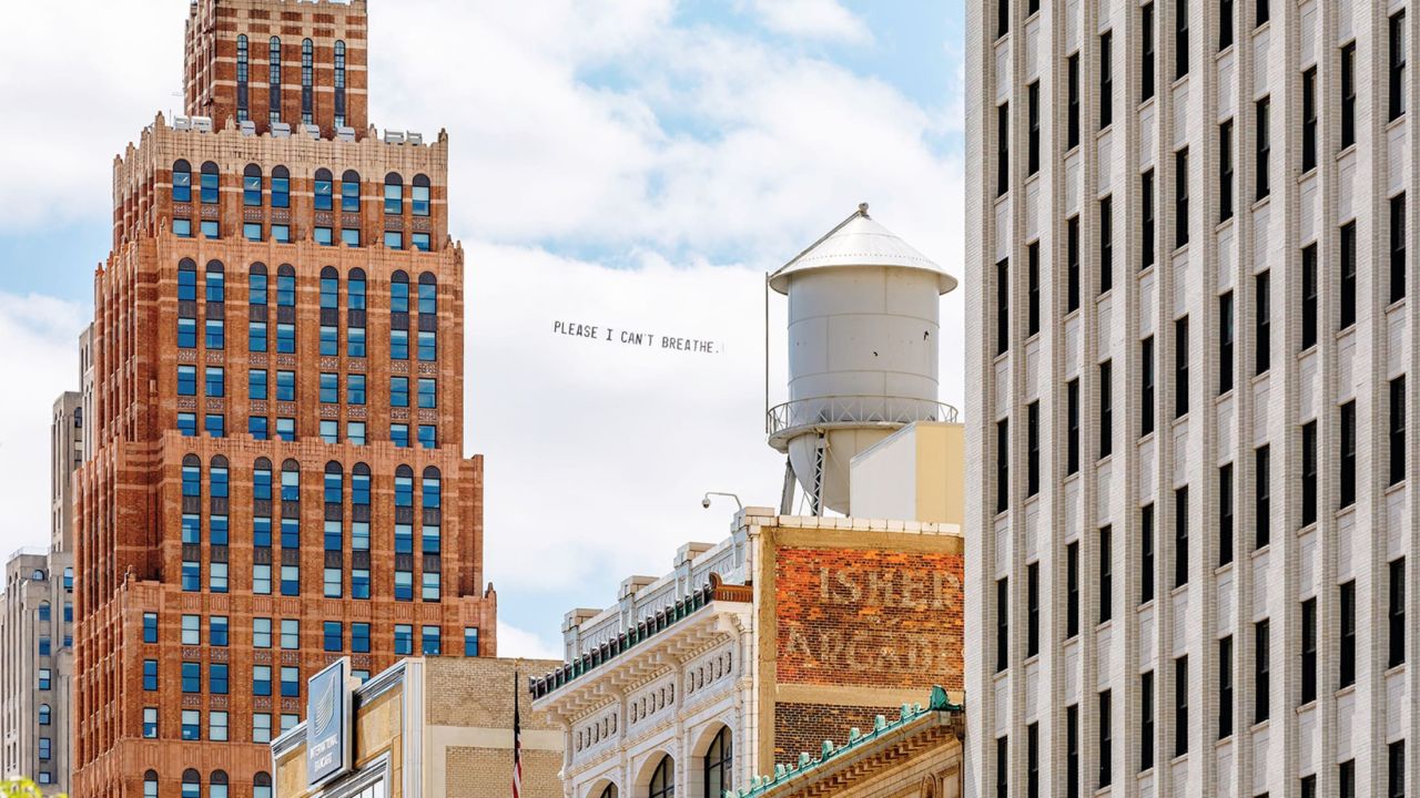 A banner reading "Please I can't breathe" flies.