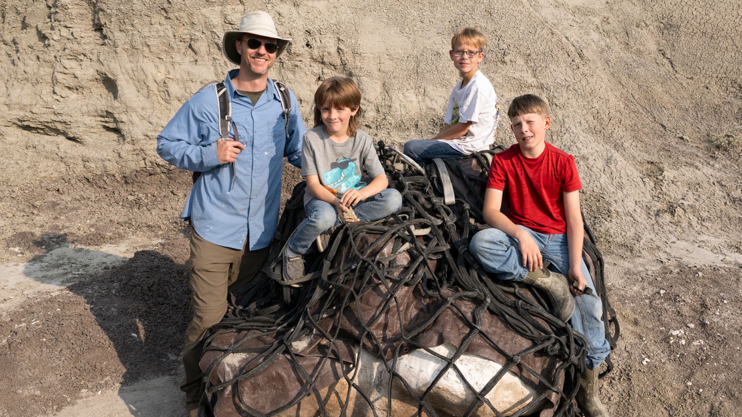 Paleontologist Dr. Tyler Lyson and fossil finders Liam Fisher, Kaiden Madsen and Jessin Fisher sit atop a helicopter net in the Badlands of North Dakota in 2023. A Black Hawk helicopter later airlifted what is believed to be a juvenile T. rex fossil after its excavation from a 66 million-year-old sandstone rock layer.