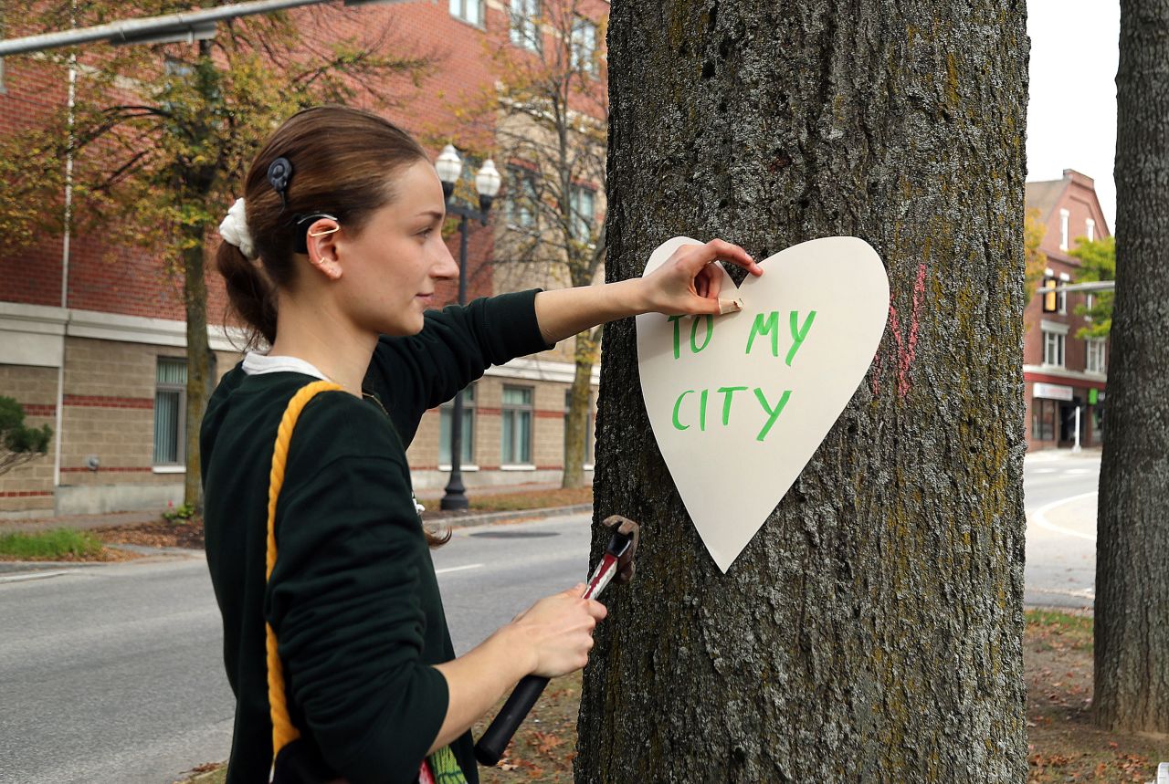 Miia Zellner nails hearts she made to trees on Main Street in Lewiston on Thursday.?