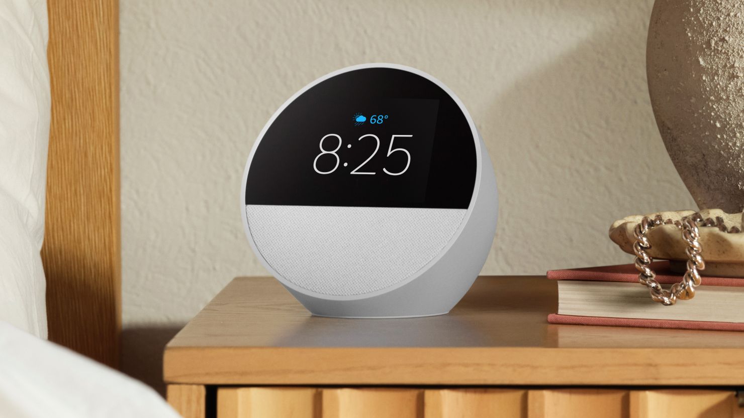 A white Amazon Echo Spot on a bedside counter reads the time of 8:25 with a forecast of 68 degrees with sun and showers.