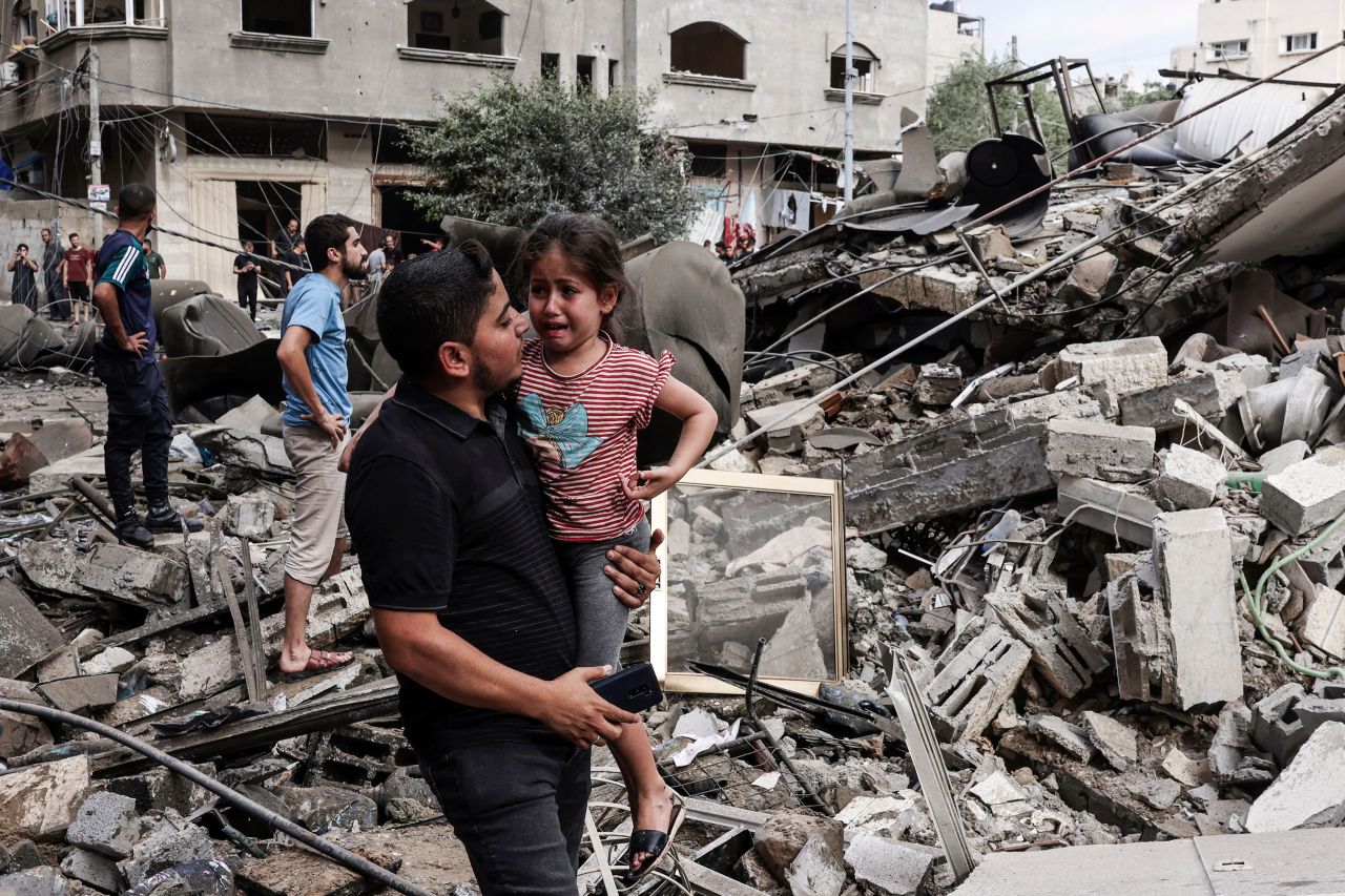 A man carries a crying child as he walks in front of a building destroyed in an Israeli air strike in Gaza City on October 7, 2023.