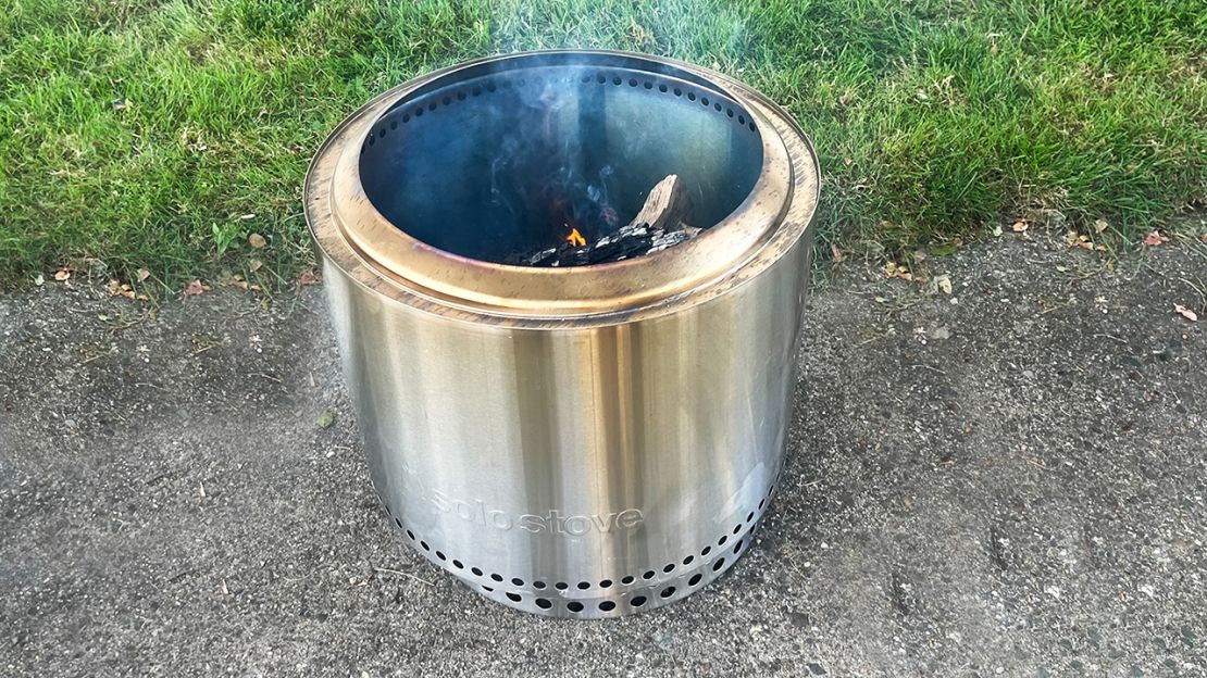 Smoke lifts off charred wood inside a stainless steel fire pit.