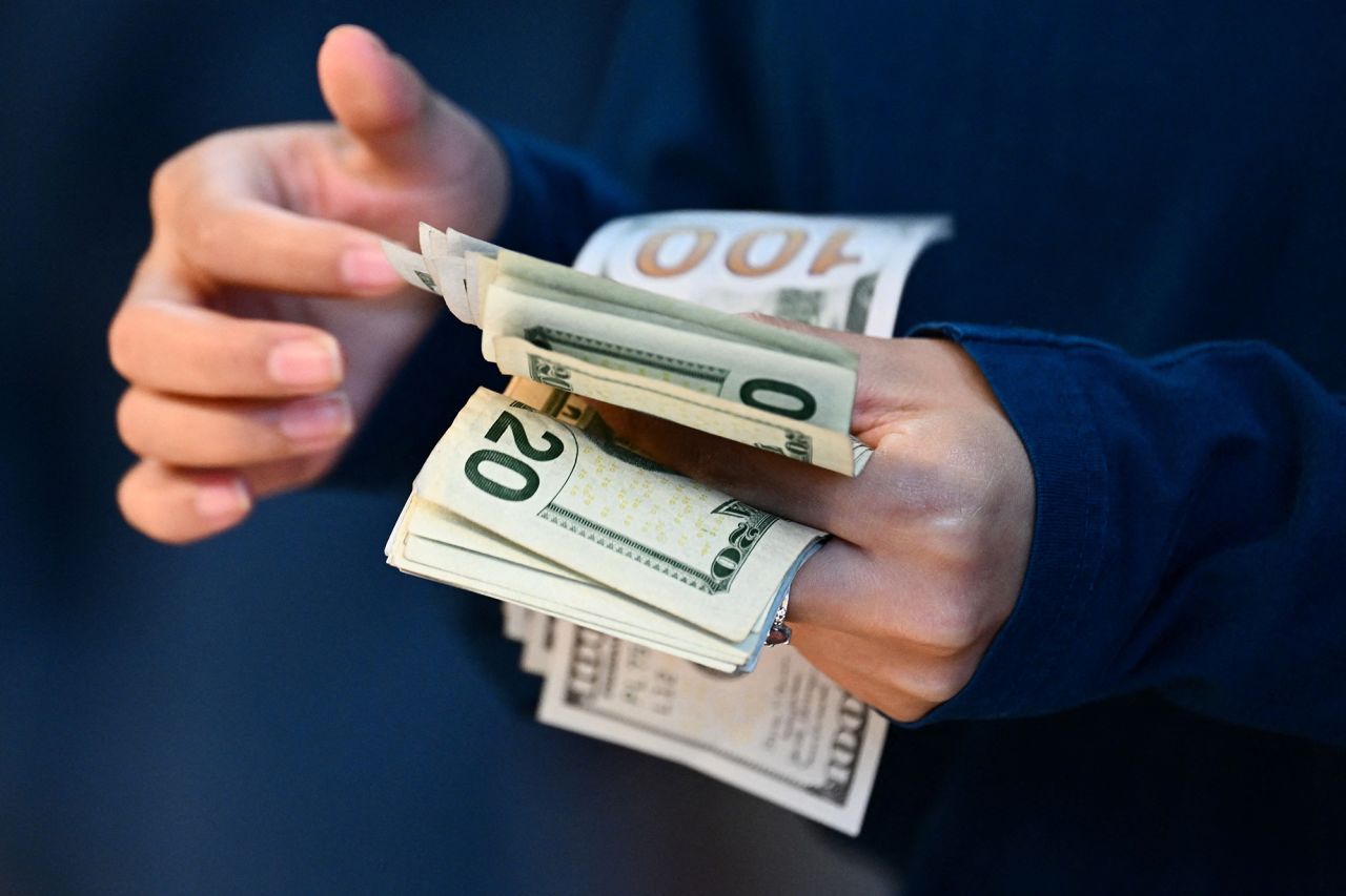 An employee counts US dollar currency as a customer pays cash for an Apple iPhone 15 series phone for sale at The Grove Apple retail store on release day in Los Angeles, California, on September 22, 2023..