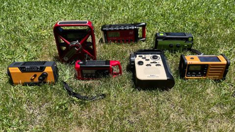 A group of seven emergency radios on a grassy lawn, charging in the sun via solar panels.