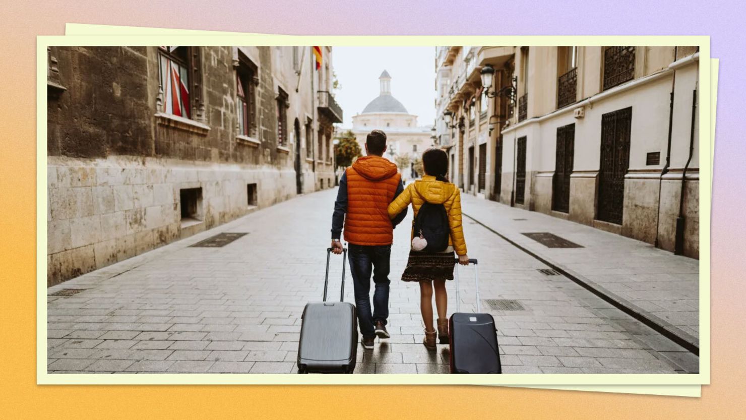 Two travelers walking down a European street with luggage