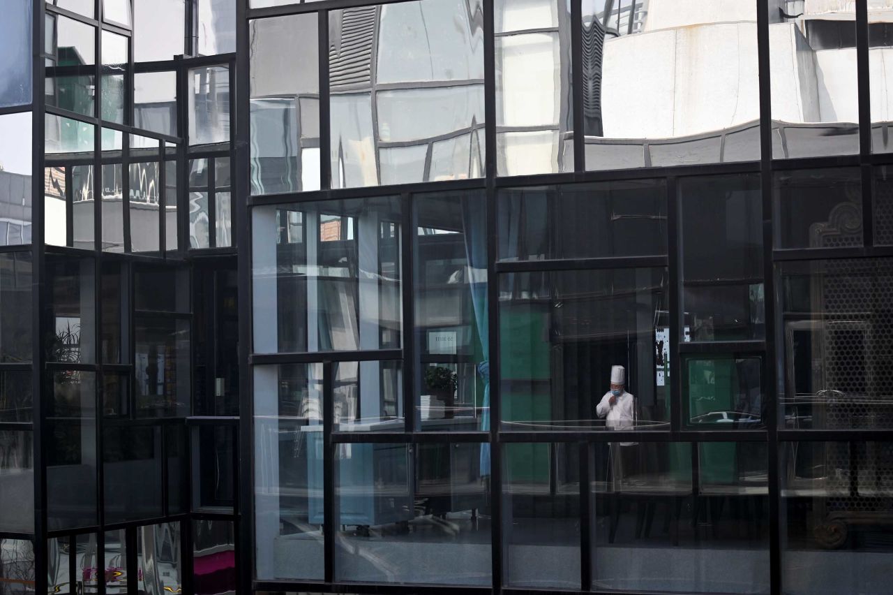 A chef wearing a face mask is reflected in a window as he pauses at the entrance to a restaurant in Beijing on Tuesday.