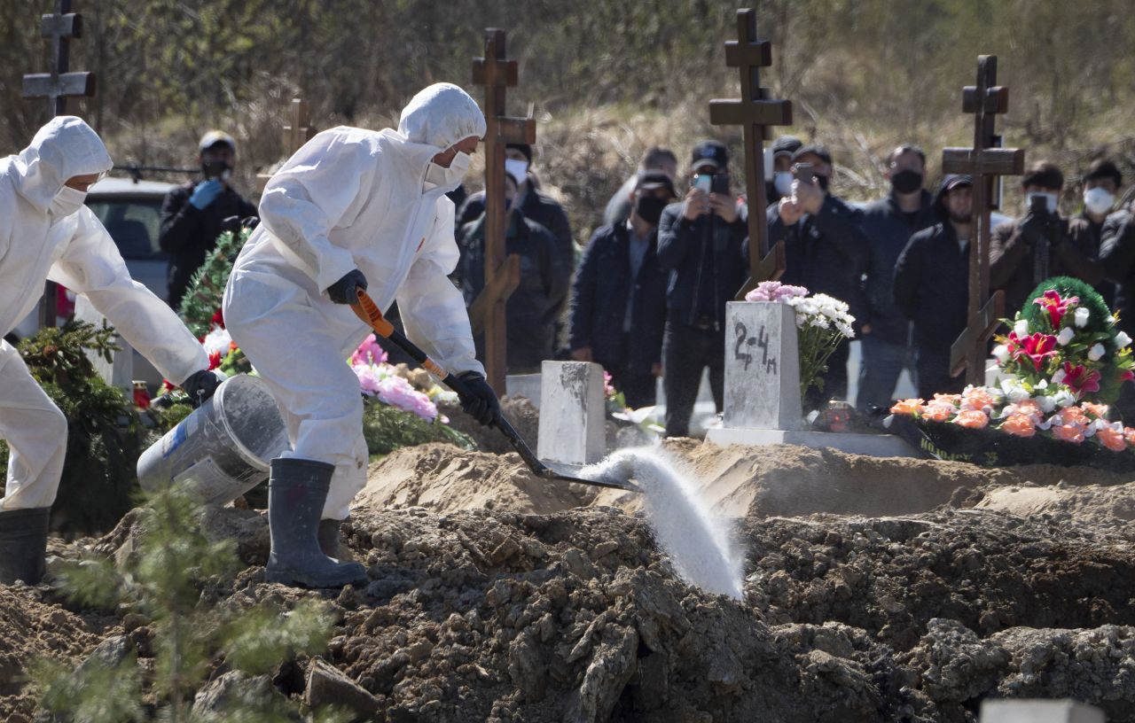 Grave diggers wear personal protective equipment (PPE) pour disinfectant on a coffin with a COVID-19 victim lowered into the grave while relatives and friends are in attendance at a cemetery in Kolpino, Russia, Sunday, May 10. 