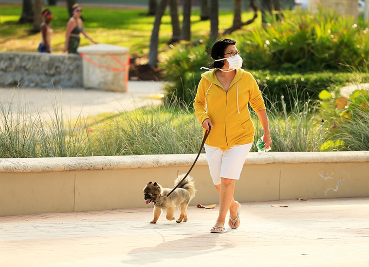 A woman wearing a mask walks her dog on the boardwalk on Thursday, April 02, in Miami Beach, Florida. 