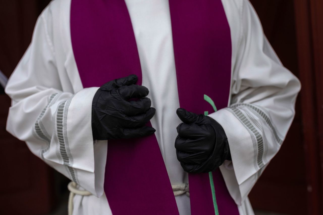 A priest wearing gloves waits in front of a cemetery chapel in Madrid on March 27.