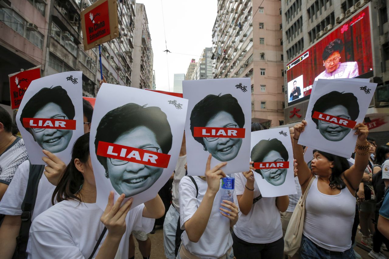 Protesters hold pictures of Hong Kong Chief Executive Carrie Lam as protesters march along a downtown street.