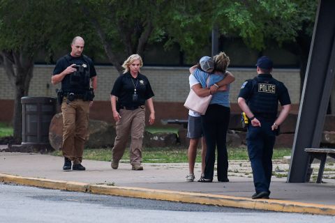 Police officers walk near people embracing at the reunion location, Memorial High School, after a shooting at the Saint Francis Hospital campus, in Tulsa, Oklahoma, June 1.