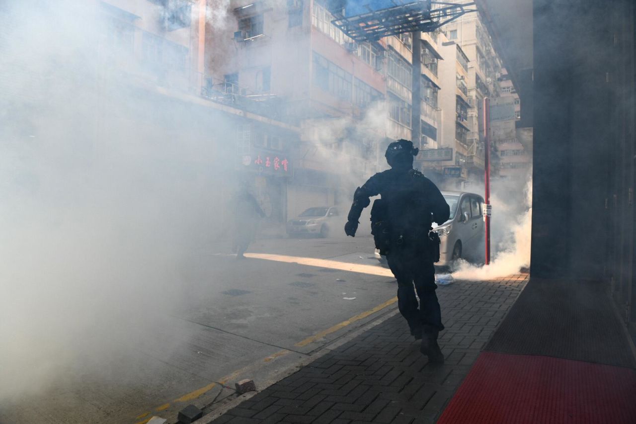 A Hong Kong police officer chases protesters through tear gas in Kowloon on Monday.