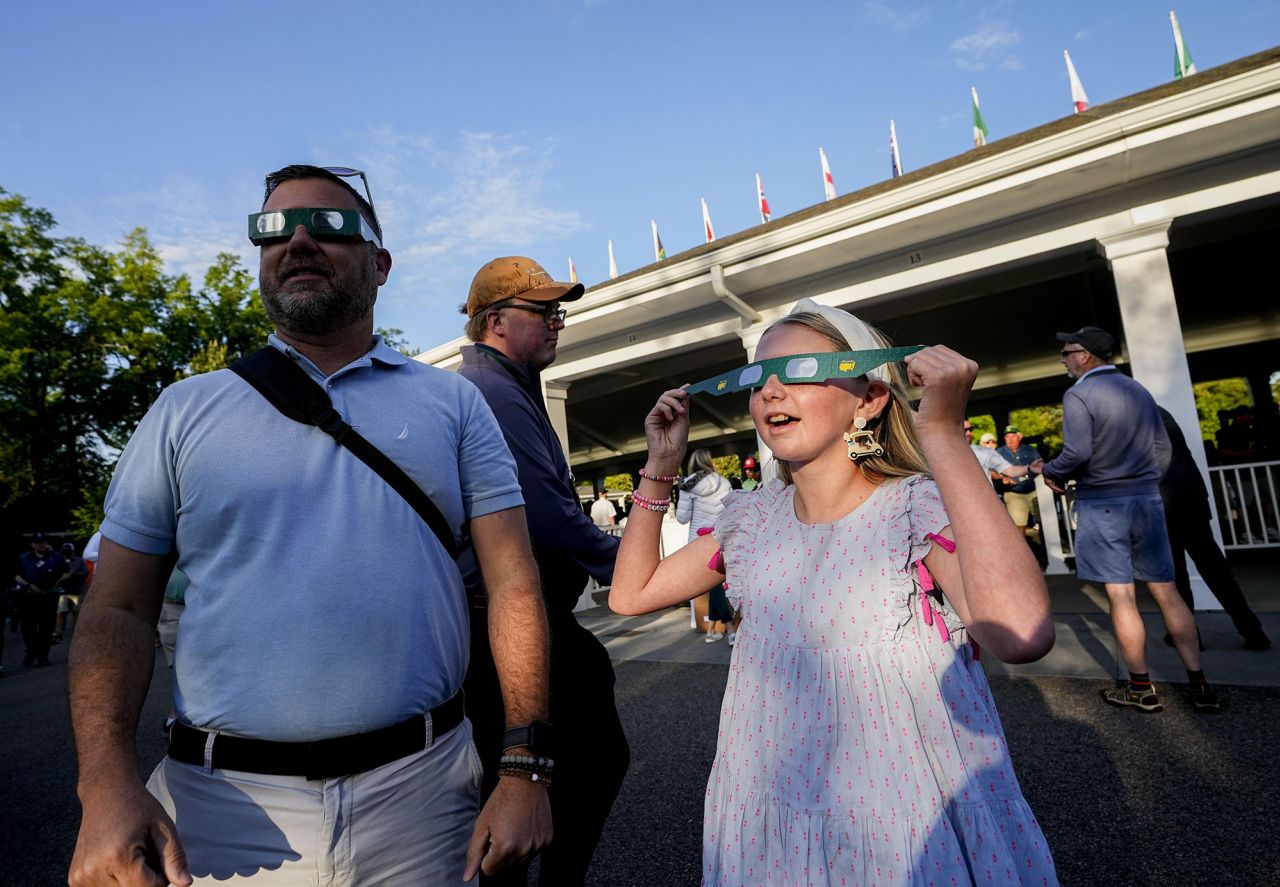 Carey Fender and his daughter, Aubrey, try on eclipse glasses during a practice round for the Masters Tournament at Augusta National Golf Club on April 8.
