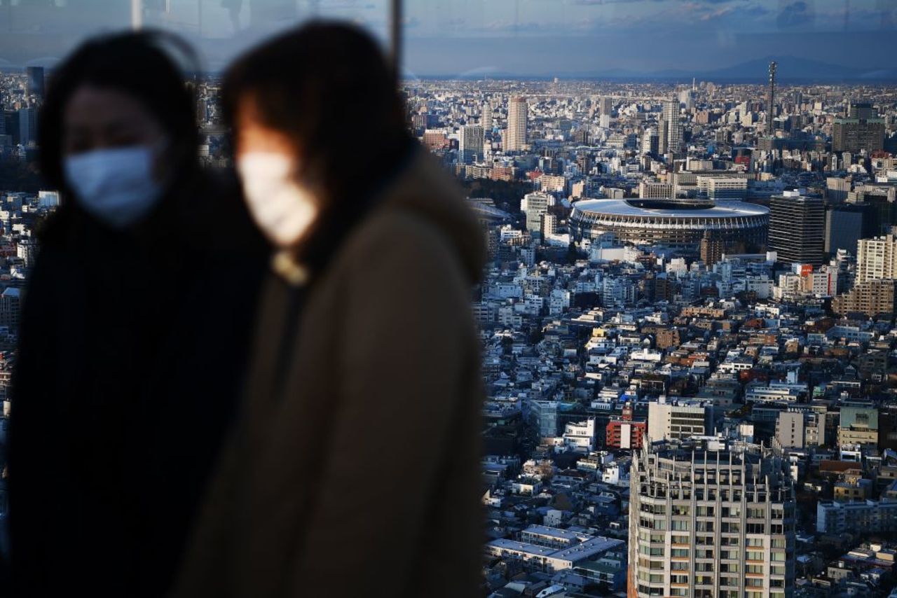 The New National Stadium, the main venue for the 2020 Tokyo Olympic Games, is seen past people wearing face masks at a rooftop viewing area in Tokyo on February 8, 2020.